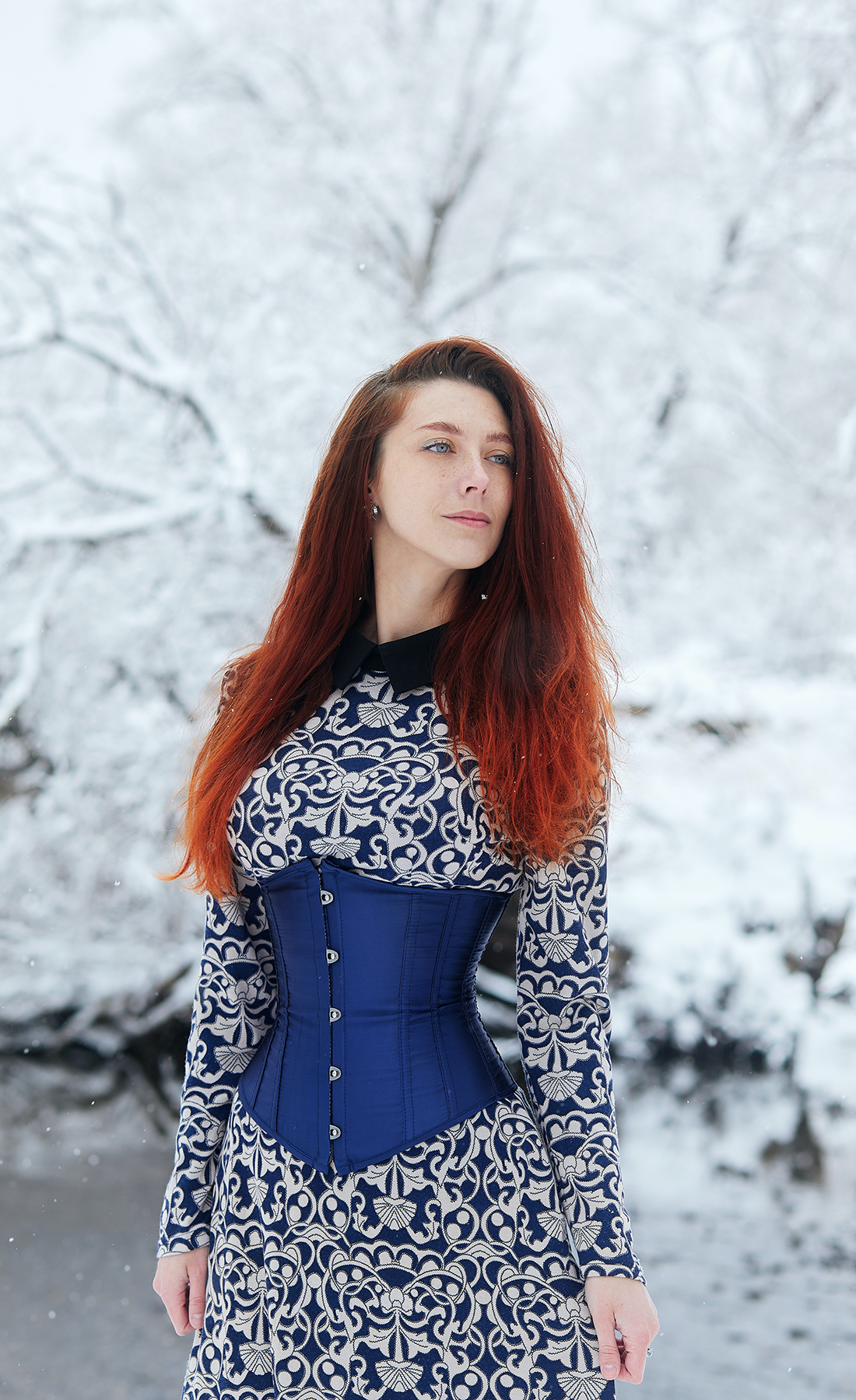 Femme portant un corset bleu se tenant dans une forêt enneigée