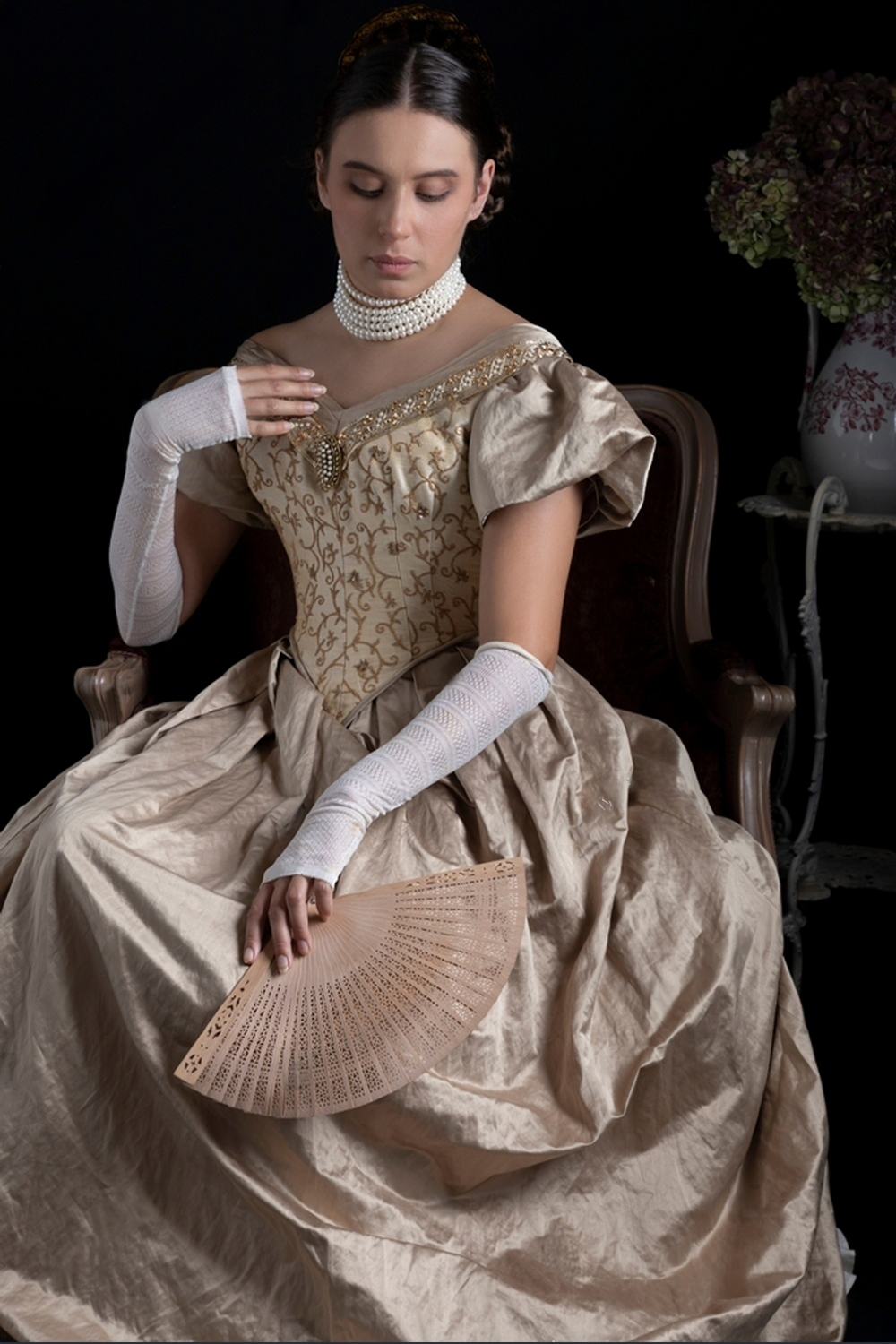 Femme assise dans un fauteuil portant un luxueux corset doré