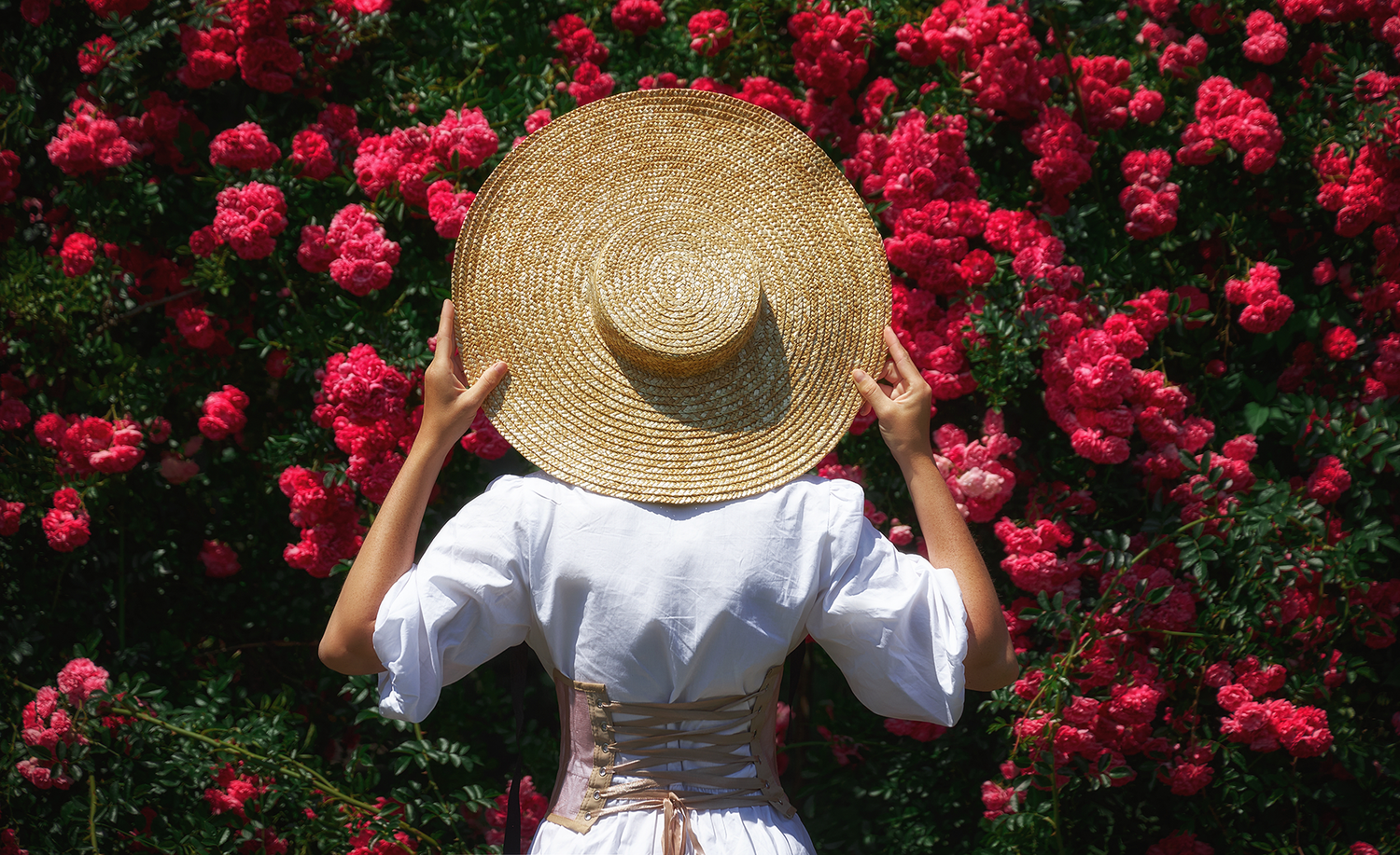 Femme portant un corset par dessus une robe blanche se tenant devant un buisson de roses