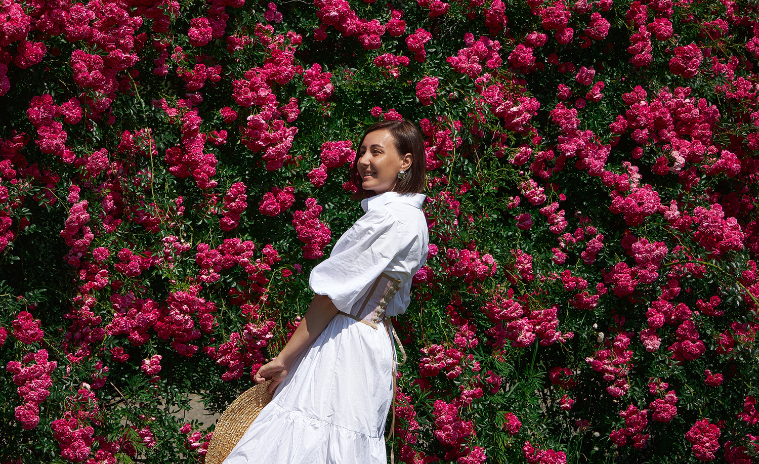 Femme portant une robe blanche et un corset se tenant devant un mur de roses